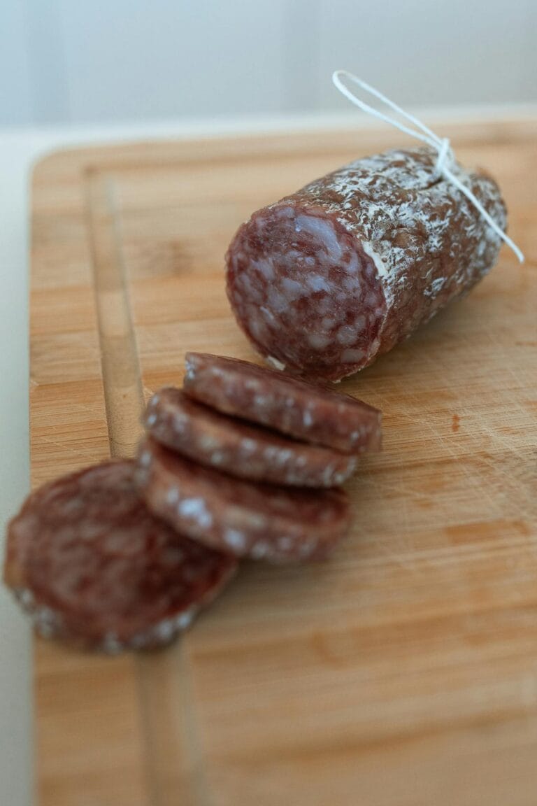 Close-up of sliced artisan salami on a wooden cutting board, showcasing gourmet delicatessen style.